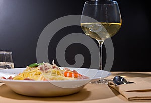 Glass with wine near delicious spaghetti pasta with shrimps, grated cheese, jamon, tomato sauce and basil in white plate