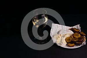 glass of wine next to a slice of cheese, plums on a black background