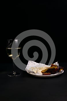 glass of wine next to a slice of cheese, plums on a black background