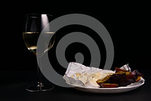 glass of wine next to a slice of cheese, plums on a black background