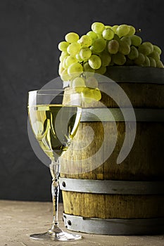 a glass of wine an oak barrel and a bunch of white grapes on a dark background