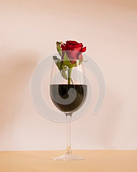 glass of wine with red rose in it on a pink beige background