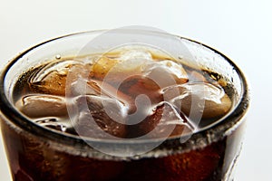 Glass wit foamy drink, soda water, coke, dark beer with ice cubes against white background.