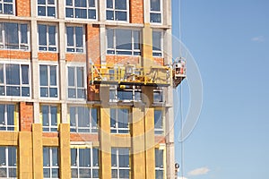 Glass wool insulation. The worker insulates the house standing on the scaffolding