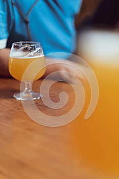 Glass of yellow weizen beer on wooden table with blurred man