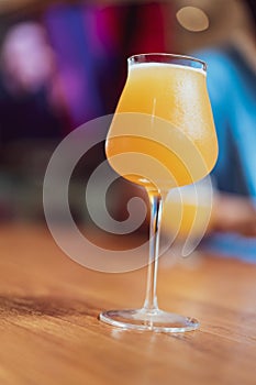 Glass of yellow weizen beer on wooden table with blurred man