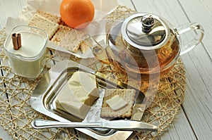 A glass of yogurt, butter, a pot of tea, pastry and fresh fruits on a light surface