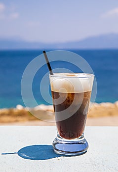 Glass of yummy iced coffee or greek freddo cappuccino on the seascape background on a summer sunny day in Kastos island