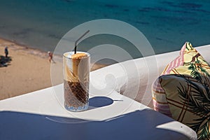 Glass of yummy iced coffee or greek freddo cappuccino on the seascape background on a summer sunny day at the Kythnos photo