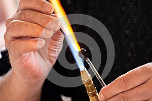 Glassblower man shaping the glass warmed by the burner flame. Close up view