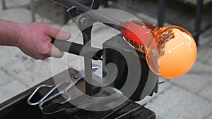 Glassblower is using wet wooden form for shaping the red melted glass on the end of glassblowing pipe. Handmade Czech