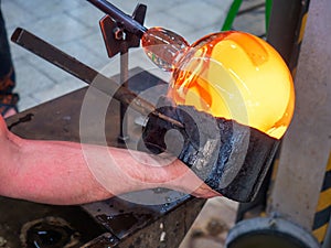 Glassblower is using wet wooden form for shaping the red melted glass on pipe