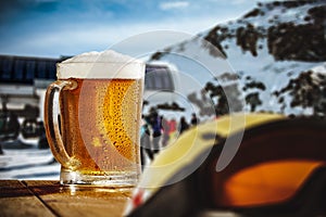 Glasse of beer on wooden table in outdoor cafe with snowy mountain background.