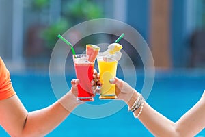 Glasse of fruit juice water melon and pineapple in hands of couple with background of turquise blue pool