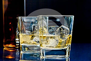 Glasses of alcoholic drink with ice on blue light