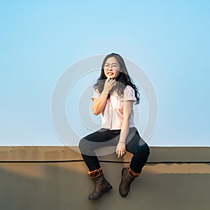 Glasses Asian woman is sitting on the rooftop barricade cement not dangerous because the opposite site is rooftop floor as well