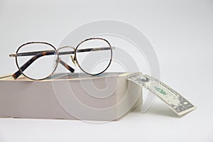 Glasses on the background of a thick book and dollar banknotes, secured old age