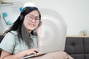 Glasses beautiful Asian woman is working on her laptop in the bedroom with a pastel green - brown color theme