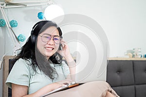 Glasses beautiful Asian woman is working on her laptop in the bedroom with a pastel green - brown color theme