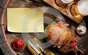 Glasses of beer, hamburger and empty paper blank on old wooden barrel. Flat layer