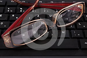 Glasses on black computer keyboard, close up