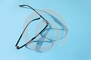 Glasses with a black frame on a blue background. Hard shadow from glasses. Vision concept