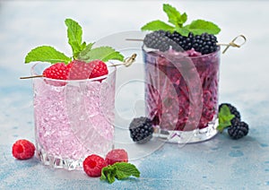 Glasses of blackberry refreshing summer cocktail and pink lemonade with ice cubes and mint on light blue background. Soda and