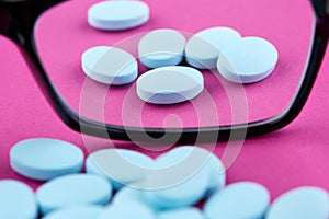 Glasses and blue pills on pink background. Medicine