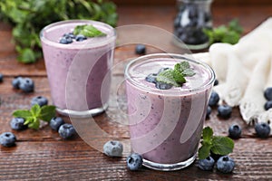 Glasses of blueberry smoothie with fresh berries and mint on wooden table, closeup