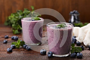 Glasses of blueberry smoothie with fresh berries and mint on wooden table, space for text