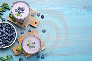 Glasses of blueberry smoothie with mint and fresh berries on light blue wooden table, flat lay. Space for text