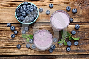 Glasses of blueberry smoothie with mint and fresh berries on wooden table, flat lay