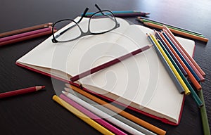 Glasses on Book with blank notebook and colored pencils