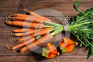 Glasses of carrot juice and fresh carrots on old wooden background, top view