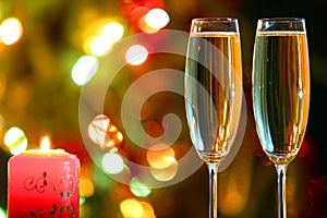 Glasses with champagne and candle against festive lights