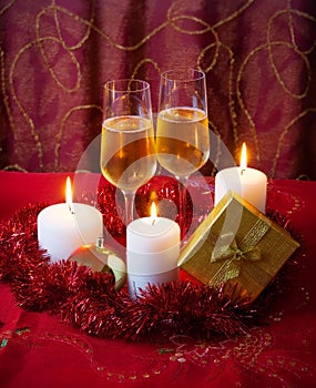 Glasses of champagne, candles, gold gift box and red tinsel