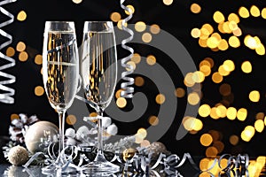 Glasses of champagne, Christmas decor and serpentine streamers against black background with blurred lights. Space for text