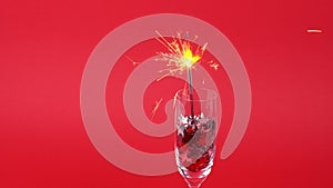 Glasses of champagne with confetti in shape of stars and sparkler on red background, Christmas decorations, copy space.