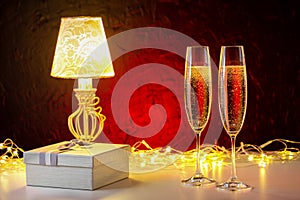 Glasses of champagne, gift box on garland light background. Romantic evening.