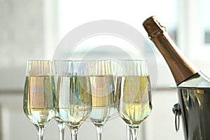 Glasses of champagne and ice bucket with bottle on blurred background