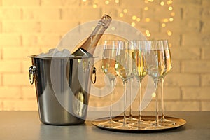 Glasses of champagne and ice bucket with bottle on grey table