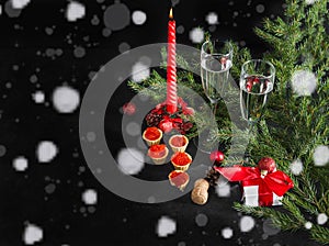 glasses of champagne. red candle, tartlets with red caviar, gift box, Christmas ball, spruce branches on a black background