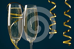 Glasses of champagne and serpentine streamers on dark blue background, closeup