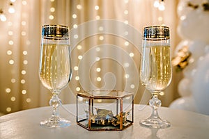 Glasses of champagne with wedding rings in a metal box and dry golden leaves. Luxury elegant wedding decor for the ceremony.