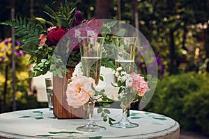 Glasses with champagne wine drink on a white wooden table decorated with white, pink and red flowers