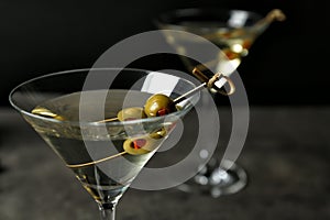 Glasses of Classic Dry Martini with olives on grey table against black background