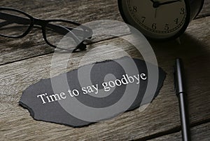 Glasses,clock,pen and a piece of black paper written with Time to say goodbye on wooden background photo