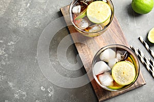 Glasses of cocktail with cola, ice and cut lime on grey background, flat lay.