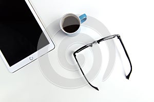 Glasses, coffee and tablet computer on white office desktop