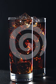 Glasses of cola with ice cubes on black stone